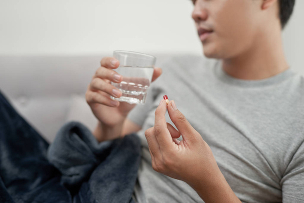 Молодой человек болен гриппом, лежит дома под одеялом, принимает таблетки
 - Фото, изображение
