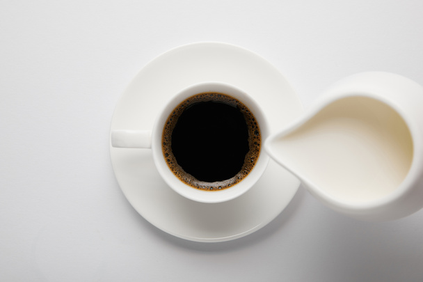 Top view of coffee cup and jug of milk on white - Фото, зображення