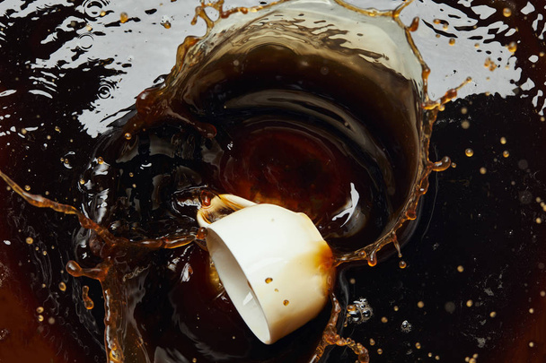 Overturned white porcelain cup with black coffee and splash - Foto, afbeelding