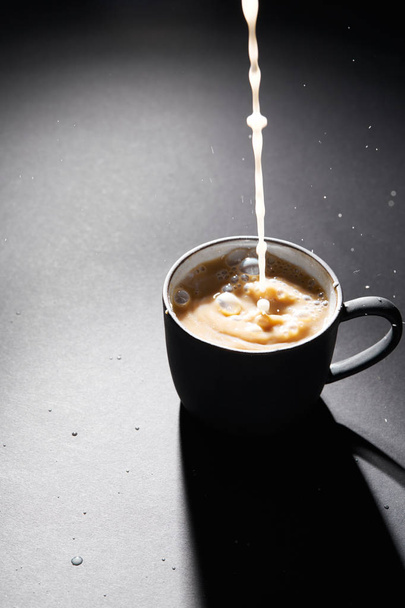 Xícara de café com leite derramando na superfície texturizada escura
 - Foto, Imagem
