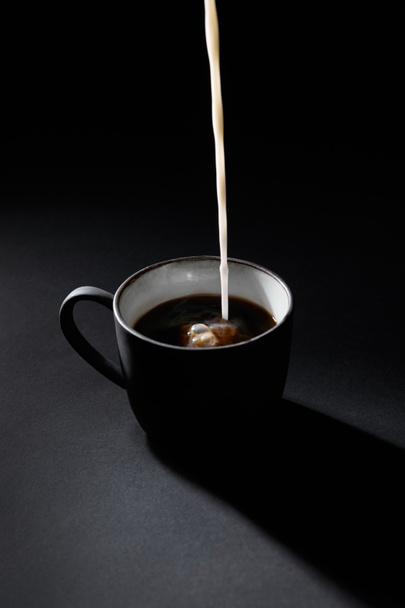 Cup of coffee with pouring milk on dark textured surface - Foto, afbeelding