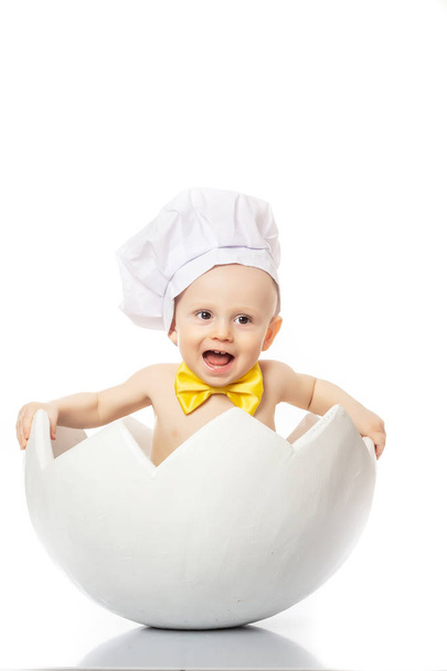 смешные детские эмоции. Маленький Шеф. Очаровательный мальчик, одетый в шляпу шеф-повара, сидит в яичной скорлупе. изолированные на белом
 - Фото, изображение