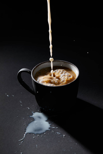 Kopje koffie met het gieten van melk op een donkere textuur oppervlak - Foto, afbeelding