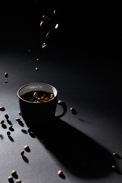 Coffee cup and coffee grains on dark textured surface - Фото, зображення