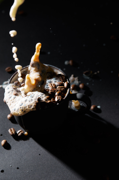 Cup of coffee with coffee grains and pouring milk on dark surface - Photo, Image