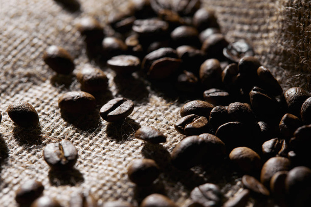 Selective focus of roasted coffee grains on sackcloth texture - Foto, afbeelding