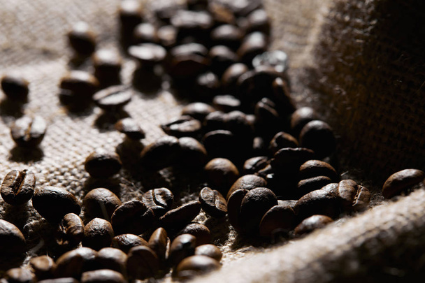 Selective focus of roasted coffee grains on sackcloth texture - Foto, afbeelding