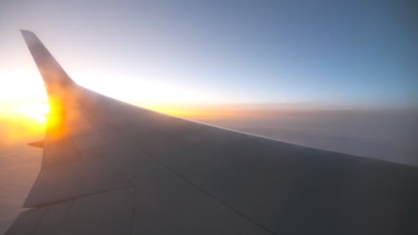 View from airplane window to sunrise or sunset. Wing of plane flying above the clouds with sun light. Aircraft flight at sky. Concept of traveling by air. Trip by airliner with beautiful background - Footage, Video