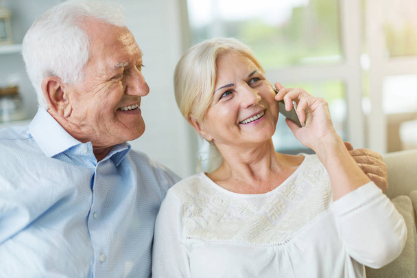 Senior couple talking on mobile phone at home - Foto, afbeelding