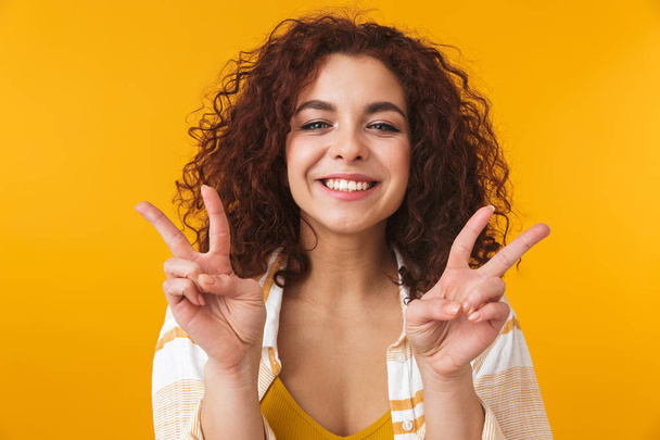 Beautiful young curly girl posing isolated over yellow wall background showing peace gesture. - Foto, imagen
