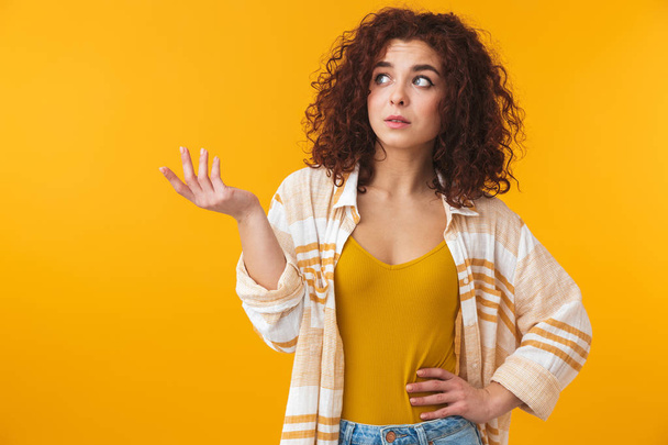 Beautiful confused young curly girl posing isolated over yellow wall background. - Photo, image