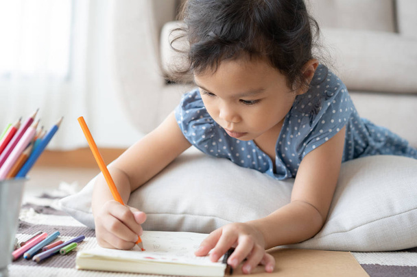 Cute little girl drawing homework and writing with pen on paper  in her home - Fotó, kép