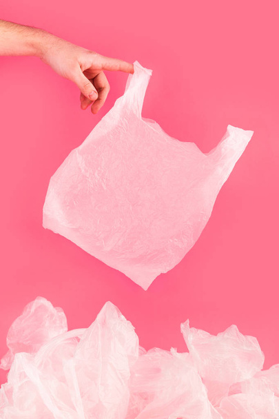 Man hand holding white empty plastic bag over a pile of crushed polyethylene. Reneissance style environment pollution concept poster. Trendy creative idea. - Фото, изображение