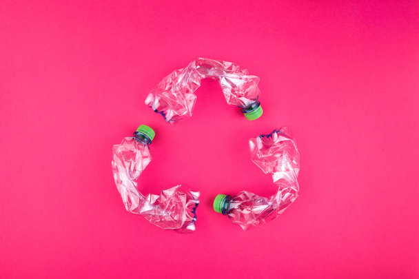 Tre bottiglie di plastica si è schiantato su brillante sfondo rosa forma segno di riciclaggio. Concetto di utilizzo della plastica. Manifesto positivo del problema ecologico attraente
.  - Foto, immagini