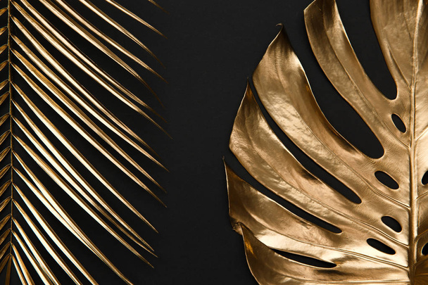 Real natural shiny monstera and palm leaves spray painted with golden metallic paint on dark deep black background. Trendy creative modern summer fashion concept. - Photo, Image