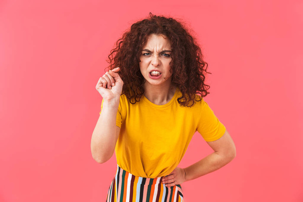 Angry beautiful young curly girl posing isolated over red wall background. - Фото, изображение