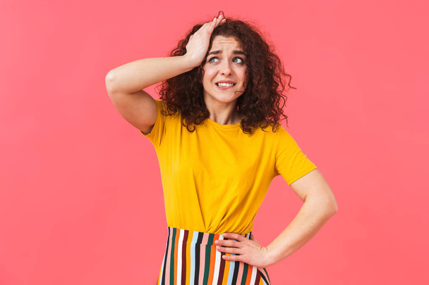 Shocked confused beautiful young curly girl posing isolated over red wall background. - Foto, Imagem