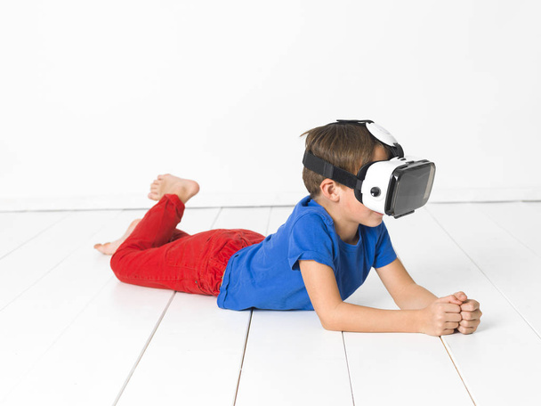 cool little boy in red trousers and blue t-shirt using virtual 3d glasses at home - Fotografie, Obrázek