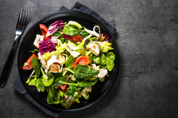 Зеленый салат с курицей и овощами на черном
. - Фото, изображение