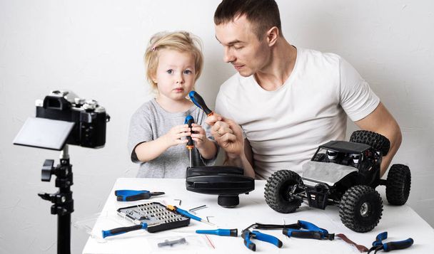 Video blogging: Dad takes a comic interview with a little daughter during the repair of a radio-controlled car buggy model. - Foto, Bild