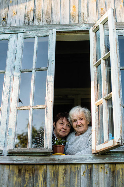 Літня жінка і її доросла дочка дивляться у вікно сільського будинку
. - Фото, зображення