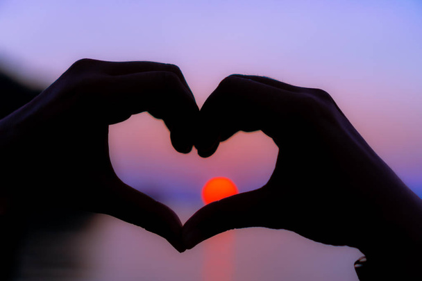 Γυναίκα χέρι καρδιά σχήμα στη φύση φόντο ηλιοβασίλεμα παραλία. - Φωτογραφία, εικόνα