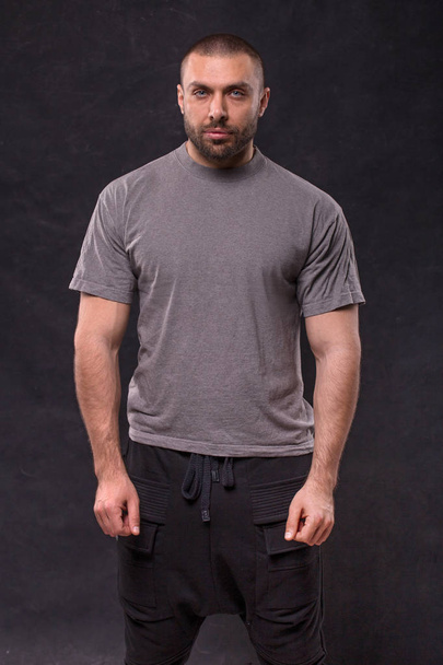 Handsome muscular beard man standing in studio over dark background - 写真・画像
