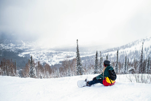 雪に覆われた斜面の山に座っている女性スノーボーダー freerider. - 写真・画像