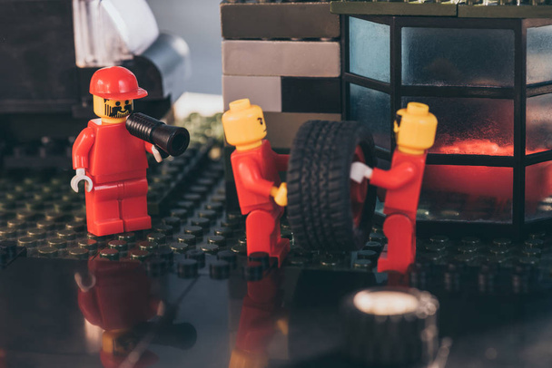 KYIV, UKRAINE - MARCH 15, 2019: lego minifigures in red carrying tire while other figurine shouting in mouthpiece at service station - Foto, Imagen