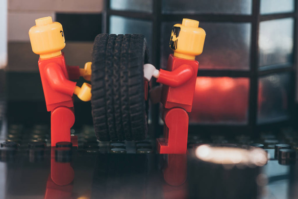 KYIV, UKRAINE - MARCH 15, 2019: close up of lego minifigures in red carrying tire on surface made of lego blocks - Photo, image