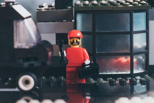 KYIV, UKRAINE - MARCH 15, 2019: red lego worker figurine in hat holding wrench and tool box near building made of lego blocks - Photo, Image