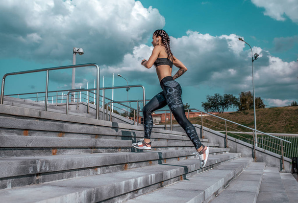 Girl athlete runs down the stairs in summer in the city In headphones, sportswear leggings top. Free space. Concept motivation, active life position, healthy lifestyle. Free space for text. - Foto, immagini