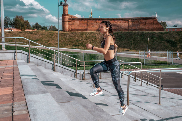 Girl athlete in headphones listening music, runs down stairs summer city, sportswear leggings top sneakers. Free space. Concept healthy lifestyle, motivation. Emotions self-confidence, strength speed. - Photo, Image