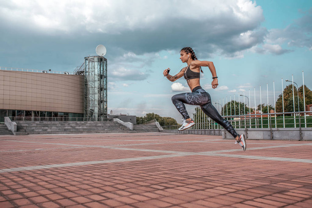 Woman jump athlete girl headphones with phone listens music, while jogging summer city, sportswear leggings top. Free space. Concept healthy lifestyle, motivation. Emotions confidence strength speed. - 写真・画像
