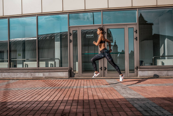 A woman runs in city in summer, a girl athlete runs, sportswear leggings top sneakers. Free space. The concept of a healthy lifestyle, motivation. Emotions of self-confidence, strength and speed. - Foto, Imagen