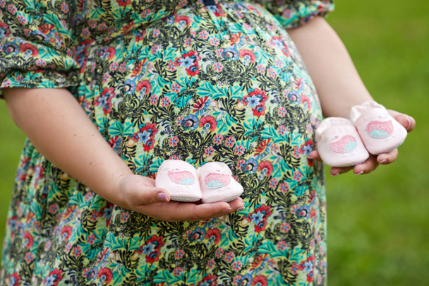 Closeup of pregnant woman holding baby shoes on her belly. Twins - Fotoğraf, Görsel