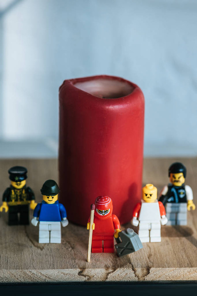 KYIV, UCRANIA - 15 DE MARZO DE 2019: Estatuilla roja con lata de gasolina y fósforo de pie con personajes lego cerca de la vela
 - Foto, Imagen