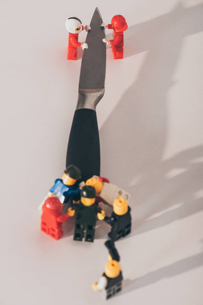 KYIV, UKRAINE - MARCH 15, 2019: close up view of plastic lego figurines carrying metal knife on white - Foto, afbeelding