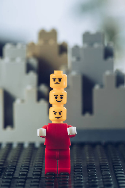 KYIV, UKRAINE - MARCH 15, 2019: red lego figurine with indifferent, smiley and angry faces on heads in front of buildings made of lego blocks - Photo, Image