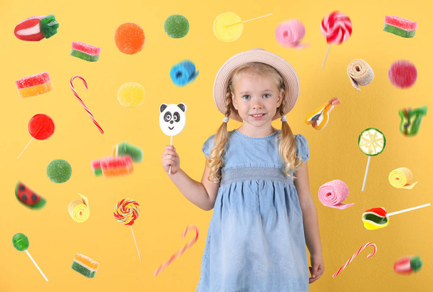 Adorable little girl with lollypop and flying candies on color background - Foto, Bild