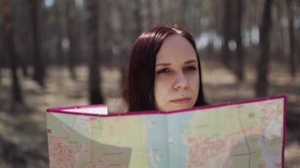Traveling woman with map in woods From below of woman with backpack sitting on log in woods reading map in sunlight - Metraje, vídeo