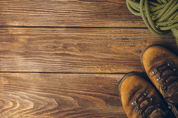 A pair of brown worn boots and a sport rope on a wooden background. Selective focus. Concept of travel and adventure. - Photo, Image