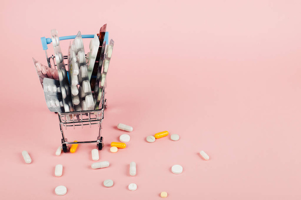 Shopping cart loaded with pills on a pink background. The concept of medicine and the sale of drugs. Copy space. - Foto, Imagem