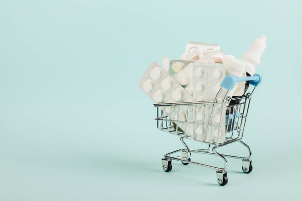 Shopping cart loaded with pills on a blue background. The concept of medicine and the sale of drugs. Copy space. - Foto, Imagem