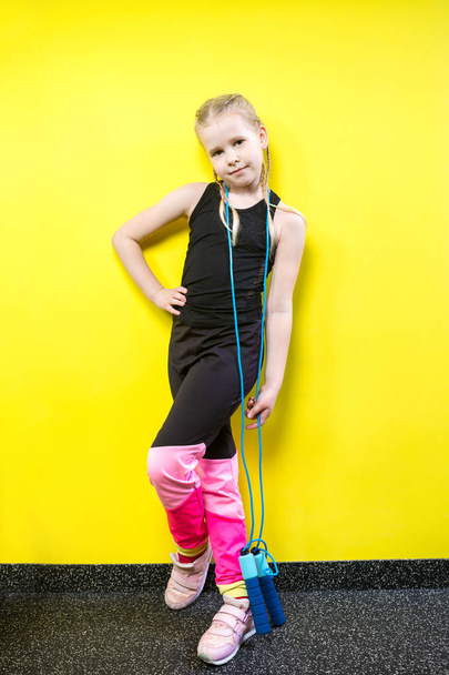Theme sport and health. Beautiful caucasian child girl with pigtails posing yellow background with smile. little athlete holds sport rope in hands. Banner advertising, space for text copy space blank - Foto, immagini