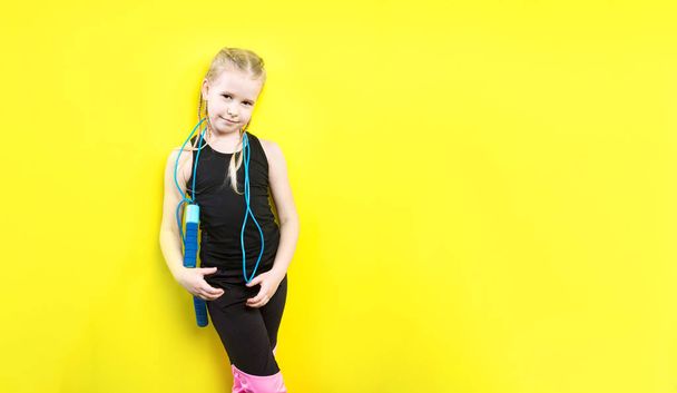 Theme sport and health. Beautiful caucasian child girl with pigtails posing yellow background with smile. little athlete holds sport rope in hands. Banner advertising, space for text copy space blank - Foto, Imagem