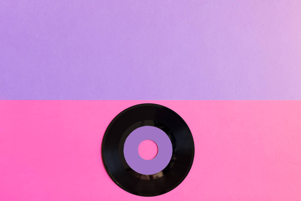 Yksi vanhentunut vinyylilevy kahden tonnin paperilla tausta: vaaleanpunainen ja violetti, pop-kulttuuri. Huippunäkymä. Minimalismi, ylhäältä katsottuna kopioi tilaa
 - Valokuva, kuva