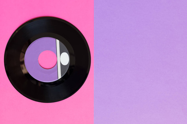 Um disco de vinil desatualizado em um fundo de papel de duas toneladas: rosa e violeta, cultura pop. Vista superior. Minimalismo, vista superior com espaço de cópia
 - Foto, Imagem
