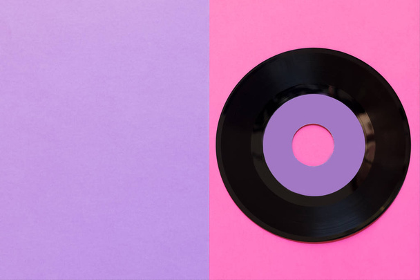 Een verouderde vinyl schijf op een twee-tons papier achtergrond: roze en violet, pop cultuur. Bovenaanzicht. Minimalisme, bovenaanzicht met kopieerruimte - Foto, afbeelding