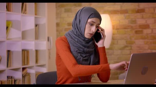 ヒジャーブ屋内オフィスのノート パソコンに入力しながら電話で会話することでイスラム教徒の魅力的な若い女性従業員のクローズ アップ撮影 - 映像、動画